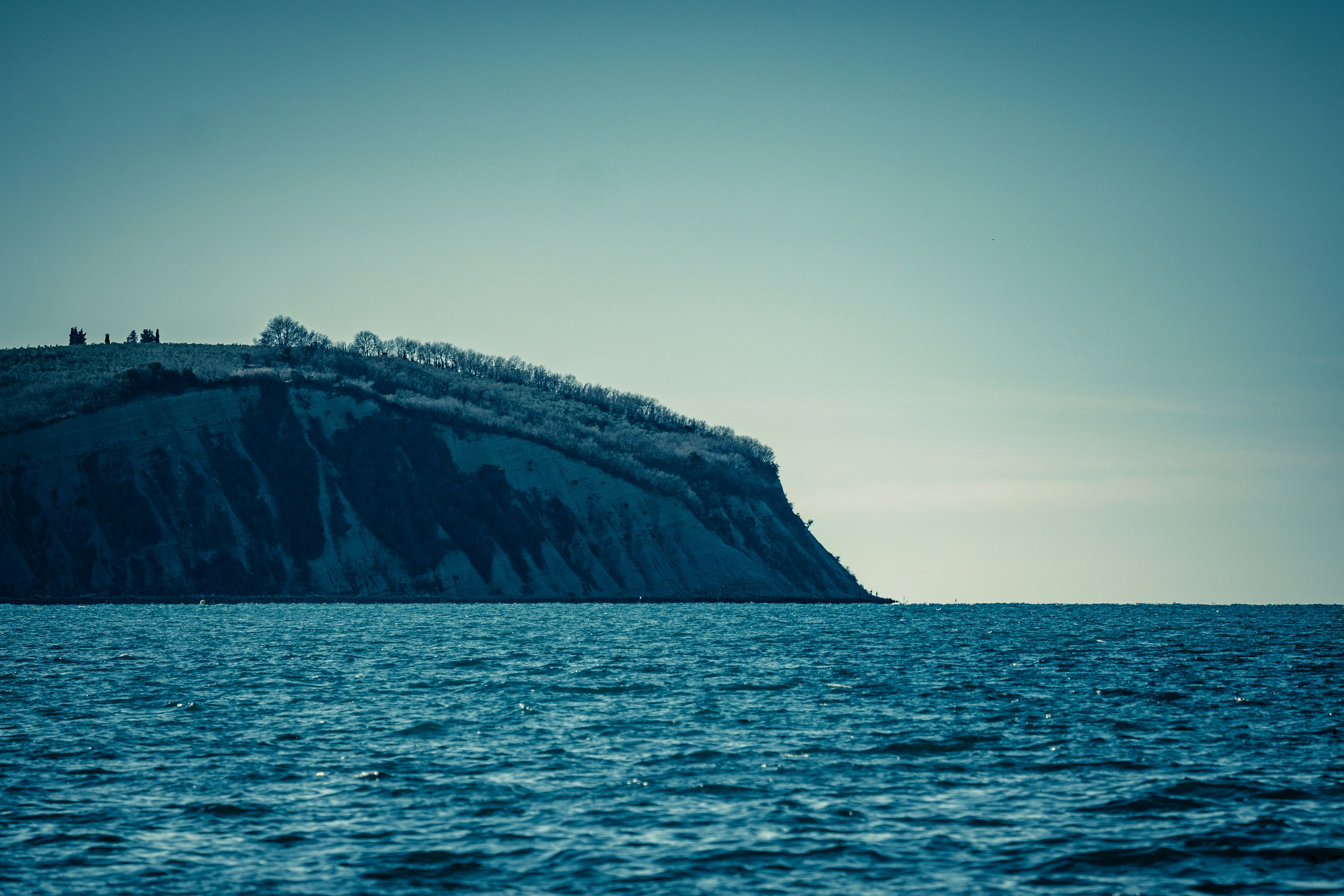 brown and green mountain beside sea during daytime